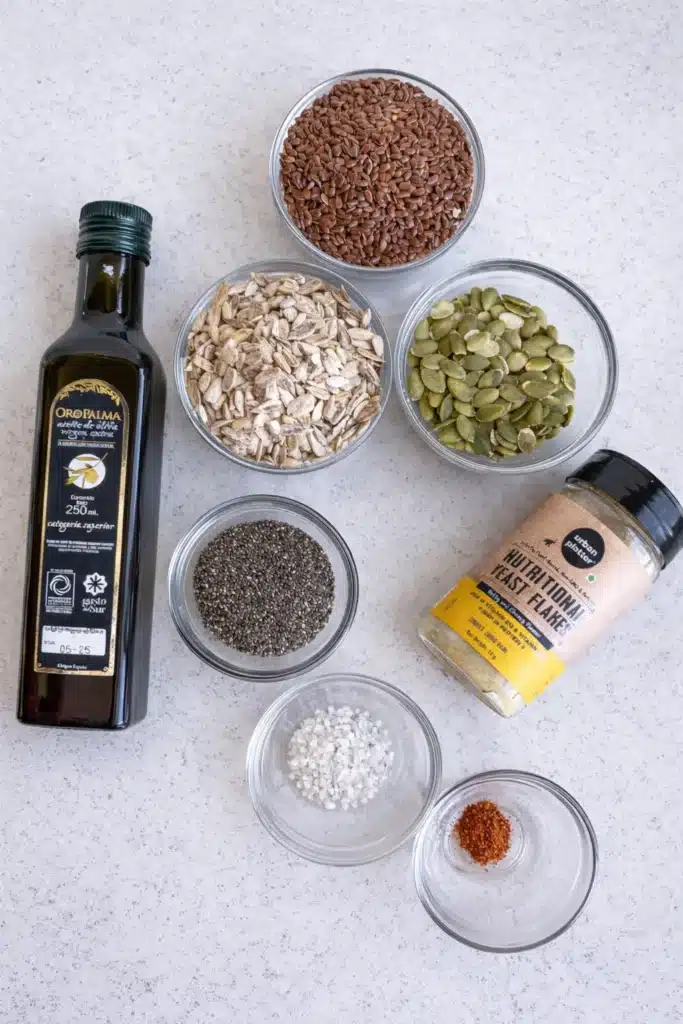 Bariatric Seed Recipe ingredients arranged in small glass bowls with flax seeds, pumpkin seeds, sunflower seeds, chia seeds, nutritional yeast, olive oil, and seasonings on a light countertop