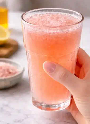 Hand holding a glass of pink salt fasting drink with lemon and Himalayan salt in the background showing that pink salt does not break a fast
