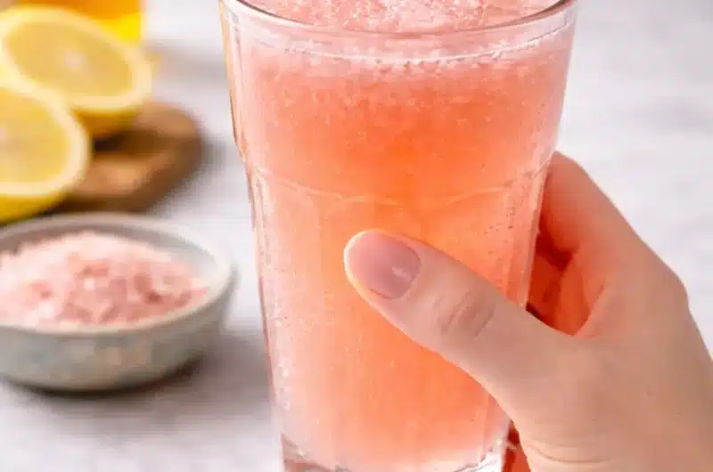 Hand holding a glass of pink salt fasting drink with lemon and Himalayan salt in the background showing that pink salt does not break a fast